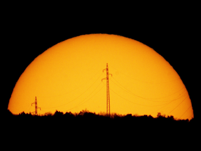 The Sun sets behind power lines.